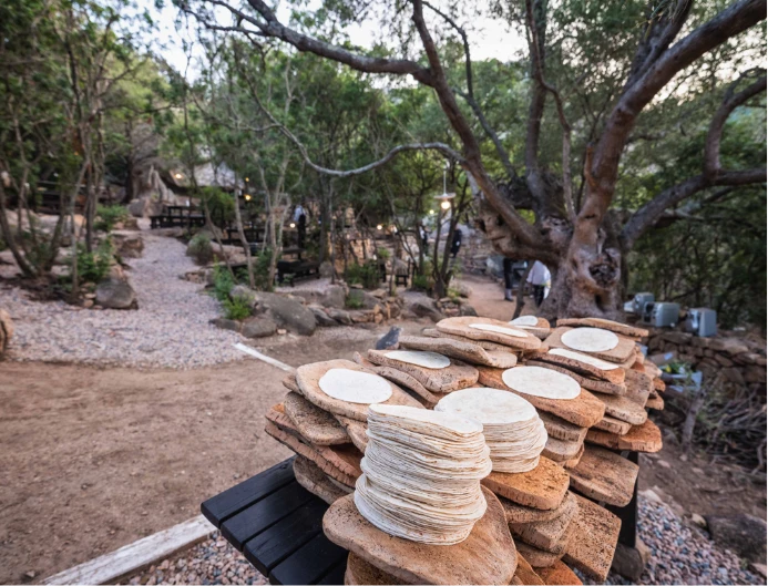 Pila di pane carasau e taglieri in sughero in un'area pranzo esterna immersa nella natura.